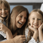 A vibrant dog park bathed in sunlight features abundant greenery with mature trees, offering ample shade for leisurely outdoor activities. In the distance is a well-equipped playground that presents an additional activity area. An inviting picnic table spreads out nearby, ideal for enjoying meals al fresco or taking relaxing breaks from play. A neatly-placed trash bin aids in maintaining the park's cleanliness for everyone's enjoyment. Dominating the scene is a generously wide dirt path gracefully curving through the expanse of grass, promising exploratory walks and lively fetch games.